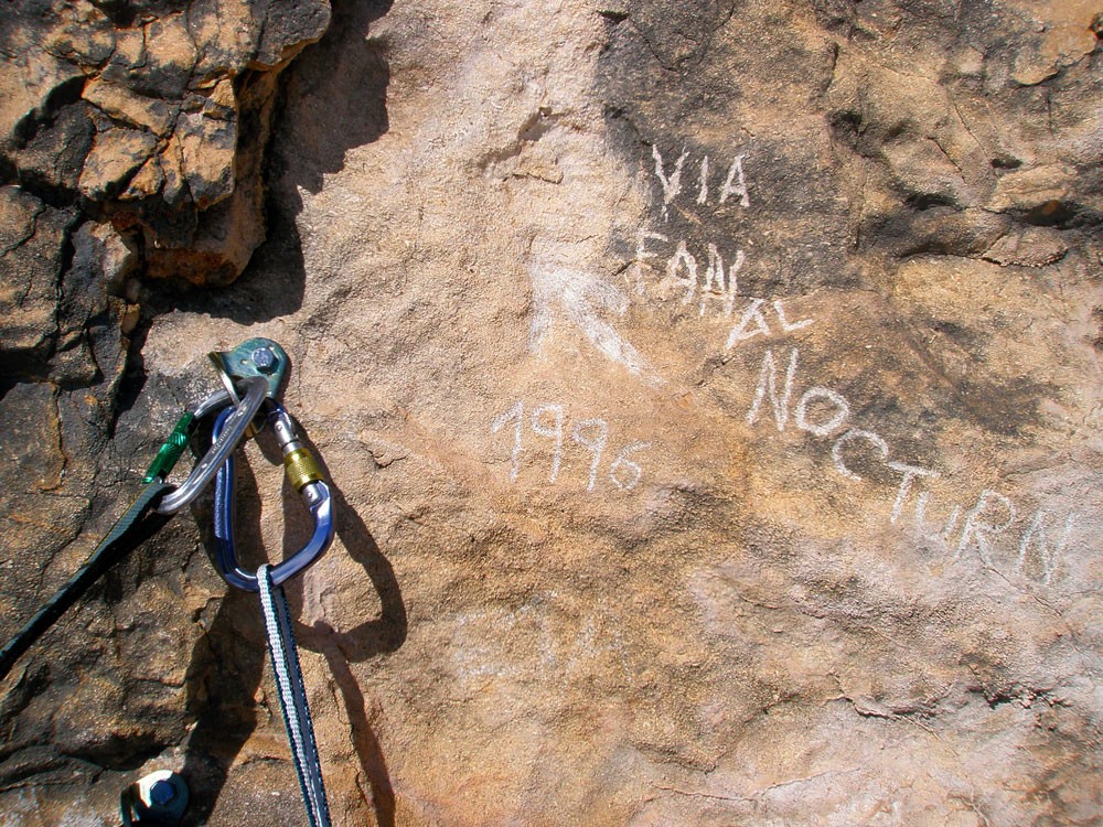 Inscripción  - Inscripción picada en la roca junto a la sexta reunión con el nombre de la vía, el año y una flecha. 